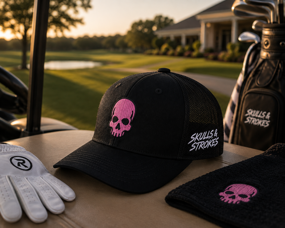 Black Skulls & Strokes Pink Skull Richardson 112 trucker hat displayed on a golf cart with golf accessories